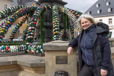 Nach der Premiere 2025 ziert auch in diesem Jahr wieder eine Osterkrone den Uthmann-Brunnen in Annaberg-Buchholz. Ivonne Schröter vom Werbering hat die Dekoration gemeinsam mit Bauhofmitarbeitern aufgebaut.