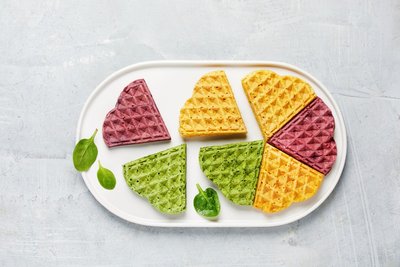 Bunte Waffeln: 180 g TK-Blattspinat, aufgetaut und abgetropft, 50 ml Öl; 3 Eier; 300 g Mehl; 1 TL Natron; Muskat. Spinat mit 100 ml Wasser und Öl im Mixer pürieren. In eine Schüssel geben, Eier unterrühren, Masse 2 Min. schaumig rühren. Mehl mit Natron und Muskat mischen und unter den Spinat rühren. Im Waffeleisen sechs Waffeln backen. Pro Waffel reichen 3 gehäufte EL Teig. Nach dem Backen abkühlen lassen. Für andere Farbe Rote Bete oder Möhren verwenden. Ergibt sechs Stück.