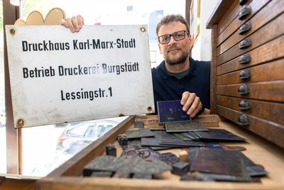René Pützschel zeigt Druckvorlagen und ein originales Schild der ehemaligen Burgstädter Druckerei. Viele der historischen Stücke finden sich heute in den Räumen des Malzirkels.