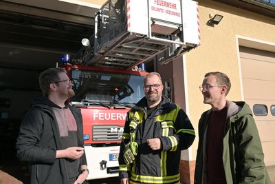 Bauverwaltungsleiter Thomas Illmann (v. l.), Ortswehrleiter Ronny Rottluff und Bürgermeister Thomas Lein an der Wagenhalle, in der sich die Feuerwehrleute während der Bauzeit umziehen - gleich neben den Einsatzfahrzeugen.