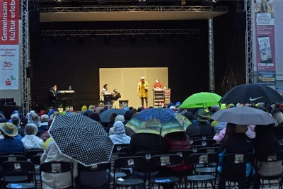 Spannung unter Schirmen beim Kabarettabend mit der Herkuleskeule Dresden in Freiberg: Dauerregen setzte nach rund 25 Minuten Spielzeit ein.