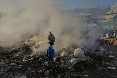 Eine Frau, die eine Tasche auf dem Kopf trägt, geht im Stadtteil Petion-Ville von Port-au-Prince an schwelendem Müll vorbei.