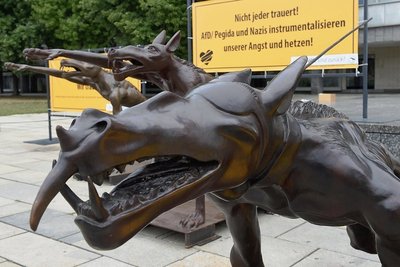 Manche der Bronzewölfe von Rainer Opolka tragen Augenklappen, manche zeigen den Hitlergruß, wieder andere sind sichtbare Mitläufer im Neonazi-Rudel. Und damit das Kunstwerk wirklich niemand falsch versteht, erklären großflächige Parolen den Hintersinn nochmal ganz genau.