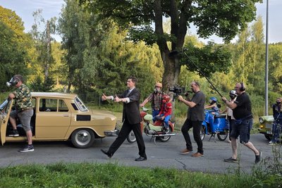 Schauspieler Michael Ransburg (Mitte) und Regisseur Heintje Peter (Zweiter von rechts) bei den Dreharbeiten am Krankenhaus in Adorf für den Film „Maske auf, Genossen“. Hier kamen mehreren DDR-Fahrzeugen und Statisten mit unterschiedlichen und lustigen Masken zum Einsatz.