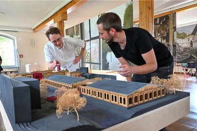 Die Projektmitarbeiter Peter Wohlwender und Antipas Papageorgiou vor einem Modell der Papierfabrik in Wolkenburg. Fotovoltaikanlagen zieren die Dächer.