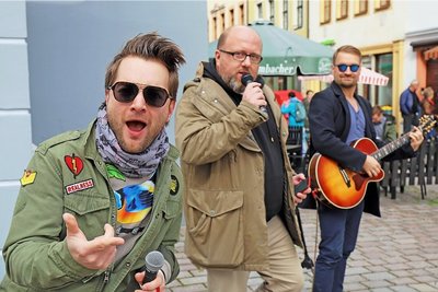 Tim Gernitz (l.) und Felix Günther (r.) von den Notendealern unterstützten Marcus Poschlod (Mitte) bei seinem Versuch, mit Gesang Geld zu verdienen. 