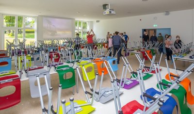 Oberlungwitzer Stadträte auf ihrem Rundgang mit Schulleiter Ronny Sieber in der Mensa im neuen Anbau der Pestalozzi-Oberschule. Sie ist mit bunten Stühlen, einem Beamer und einer Leinwand ausgestattet.