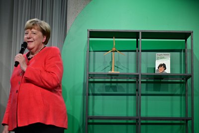 Angela Merkel (CDU), Bundeskanzlerin a.D. und ehemalige Bundesumweltministerin, spricht auf der Bühne beim Festakt "Seit 40 Jahren NaturVerbunden" zum 40. Jubiläum des Bundesumweltministeriums im Café "Moskau", während im Hintergrund ihr Buch mit dem Titel „Der Preis des Überlebens“ zu sehen ist.