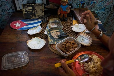 Eine Angestellte eines Souvenirgeschäfts in Havanna isst neben Bildern von Che Guevara, Fidel Castro und Ernest Hemingway.