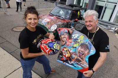 Mandy und Arne präsentieren zwei der von Marquez signierten Preise, welche die Sachsenring-Zuschauer am Wochenende bei einer Tombola für den guten Zweck gewinnen können.