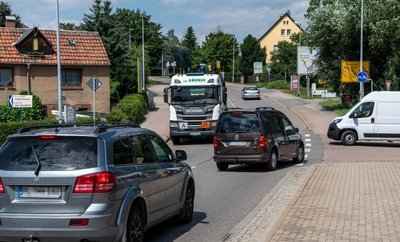 Auf der innerörtlichen B 107 verkehren auf Höhe der Poppitzer Senke zahlreiche Autos, Transporter und Lastwagen. Aufgrund einer Bäckerei und eines Discounters queren viele Menschen die Straße. 