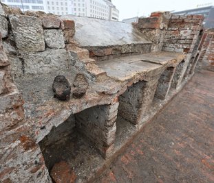 Die Nischen in der Wand eines Kellers, der zum "Goldnen Anker" gehörte, sollen als Weinregale gedient haben. Weinflaschen wurden bei den Grabungen jedoch nicht gefunden. Die Schräge auf der Mauer gehörte zu einem Fenster. Im Vordergrund sind zwei Schuhe zu sehen, die möglicherweise Kellnern gehört haben könnten.