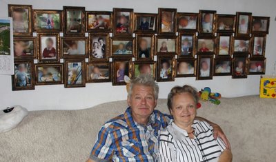Rosi und Peter Fischer vor den Fotos ihrer Pflege- oder Adoptivkinder, denen sie in schwierigen Zeiten als Pflegeeltern zur Seite standen. Die Gesichter der Kinder wurden von der Redaktion aus Gründen des Persönlichkeitsschutzes unkenntlich gemacht.