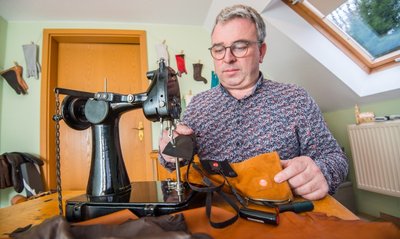 Handschuhmacher Rico Wappler an seiner Nähmaschine. Vor sich hat er einen der Spezialhandschuhe. Der Akku steckt hinter einem Reißverschluss an der Seite, das schwarze Band ist das Heizelement. 