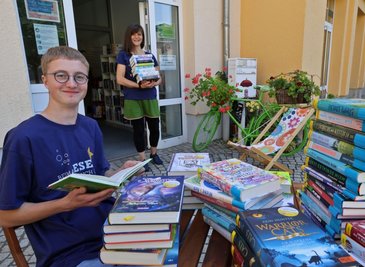 Stapelweise neue Jugendbücher gibt's beim Buchsommer in der Stadtbibliothek Lichtenstein. Timon Grießbach (links) sichtet im Büchergarten die Lektüre. Im Hintergrund Mitarbeiterin Peggy Hartmann. 