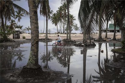 Nach dem Sturm ist vor dem Sturm: Ein Junge radelt über ein geflutetes Gelände eines Atolls, das zu Tuvalu in der Südsee gehört. Das Wasser holt sich immer mehr Land. Manche der alten Kokospalmen könnten beim nächsten Unwetter ein Opfer des Meeres werden.
