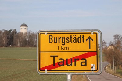 Auf einer Bildmontage eines Ortsausgangsschildes von Taura wird die Entfernung zu Burgstädt gezeigt.