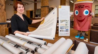 500 Jahre Marienberg: Bergstadt beleuchtet Handelsgeschichte - Susann Hofmann, Amtsleiterin für Kultur und Tourismus der Stadt Marienberg, zeigt gemeinsam mit Fest-Maskottchen Uli zwei der insgesamt 78 zur Marienberger Handelsgeschichte entstandenen Banner.