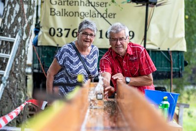 Dietmar Groß aus Pleißa versucht sich an der "Bierrutsche" beim Teichfest im Limbach-Oberfrohnaer Ortsteil Dürrengerbisdorf. Der 71-Jährige ist mit seiner Lebensgefährtin bereits zum wiederholten Mal zu Gast bei der Veranstaltung. Bei dem Spiel muss ein gefüllter 1-Liter-Maßkrug auf einer zehn Meter langen, mit Seifenwasser benetzten Holzbahn so weit wie möglich geschoben werden, ohne dass das Glas am Ende zu Boden stürzt. Gewonnen hat, wer der Zehnmetermarke am nächsten kommt. Dietmar Groß schaffte am Samstagnachmittag mit 9,71 Meter bereits einen beachtlichen Wert.