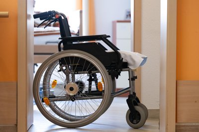 Ein Rollstuhl steht in einem Altenheim vor einem Zimmer.