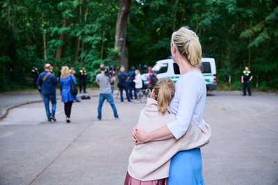 Löwenjagd in Kleinmachnow: Eine Anwohnerin und ihre Tochter sehen dem Treiben von Journalisten und Polizei zu, während Tierexperten und Polizeibeamte in einem Waldgebiet in Zehlendorf stehen.