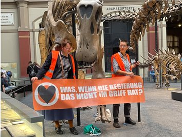 Zwei Klimaaktivistinnen mit einem Banner "Was, wenn die Regierung das nicht im Griff hat?" haben sich im Berliner Museum für Naturkunde an den Haltestangen eines Dinosauriers festgeklebt. 