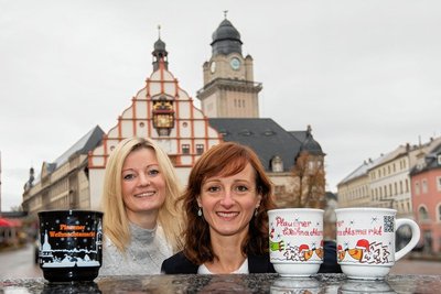 Hoch die Tassen: Sophie Gürtler vom Stadtmarketing und Anja Linke aus der Pressestelle der Stadt zeigen die Glühweintassen von 2021 (weiß) und aus dem Jahr 2020. Im Rathaus stapeln sich wegen coronabedingter Weihnachtsmarktpause die Henkelbecher.