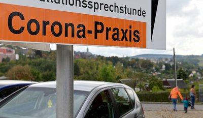 Vor der Stadtkulisse mit der Kirche St. Annen ist das Schild einer Corona-Praxis zu sehen. 