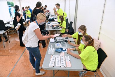 Eine Probandin (vorne, links) steht vor Beginn eines Großversuchs der Universitätsmedizin Halle/Saale am Check-In.