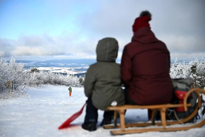 Oberwiesenthal am Samstag: Ausflügler sitzen auf einem Schlitten auf dem Gipfel des verschneiten Fichtelberges. Im Bergland fällt auch in den kommenden Tagen Schnee.