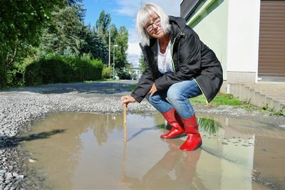 Margit Oettel misst mit dem Zollstock: Auch Tage nach einem Regen ist die Pfütze noch bis zu zehn Zentimeter tief. 