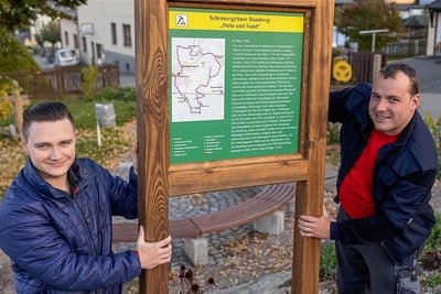 Lucas Linder (links) und Nils Fischbach vom Förderverein Feuerwehr Schreiersgrün montieren die Infotafel zum Rundwanderweg auf dem Dorfplatz am Feuerwehrdepot. Dort beginnt die 7 Kilometer lange Tour "Stein und Sand".