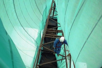 Innerhalb der Planen müssen die Arbeiter auf dem Mast neben der normalen Sicherheitsausrüstung Schutzanzüge und Schutzmasken tragen.
