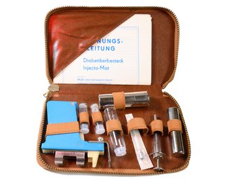 Ein Diabetikerbesteck von Ende der 1970er-Jahre aus der DDR: Es enthielt die damals in Serienreife gegangene Spritzpistole, die Spritze zur Mehrfachverwendung, daneben eine verschließbare Metallhülse zur Aufbewahrung der sterilisierten Spritze, Glasbehälter zur getrennten Aufbewahrung steriler und gebrauchter Kanülen und ein Behälter mit Desinfektionslösung.
