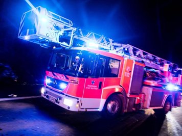  
          Ein Drehleiterwagen der Feuerwehr fährt mit Blaulicht an einer Unfallstelle vorbei.