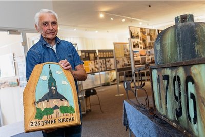 Ortschronist Günter Bäuerle mit einem geschnitzten Relief zum Kirchenjubiläum. Rechts die historische Wetterfahne und die alte Turmkugel.