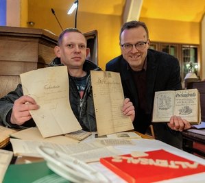 Der Grünbacher Ortschronist Jan Hartmann Ortschronist (links) und Pfarrer Jörg Grundmann mit einem alten Gesangsbuch und Kaufurkunden zum Friedhof. 