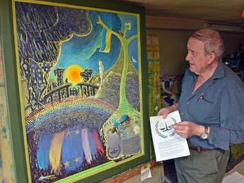 Künstler Werner Franz in seinem Atelier in Grumbach, wo er derzeit ein Werk zum Thema Russland-Ukraine-Krieg fertigstellt. In der Hand hält er eine Beschreibung des Signets des Europäischen Gerichtshofs für Menschenrechte, welches er in das Triptychon einarbeitet.
