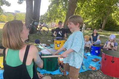 Hinten sitzt Marleen Kiesel vom Community-Music-Projekt "Paper lantern" an der Trommel und musiziert mit Kindern in der Zwergstadt.