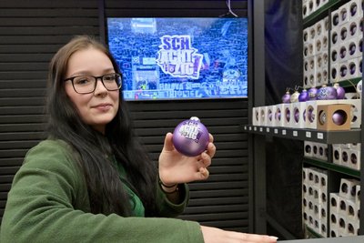 Laura Müller, Mitarbeiterin bei Gebrüder Roth, zeigt die Jubiläumsausgabe der FCE-Weihnachtskugel „Schachtzig!“.