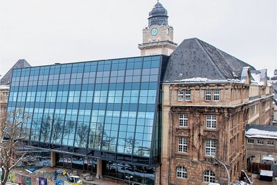 Bewegung hinter dem farbenfroh gestalteten Bauzaun. Die Glasfassade des Rathauses ist fertig, die Arbeiten im Inneren des Gebäudes dauern noch an.