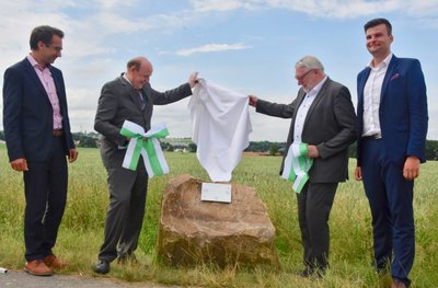 Jens Hinkelmann und Landrat Christoph Scheurer vom Landkreis Zwickau sowie Mittelsachsens Landrat Matthias Damm und Steve Sarfert, stellvertretender Mühlauer Bürgermeister (von links), enthüllen einen Findling. Er soll die neu gezogene Landkreis- und Gemeindegrenze zwischen Zwickau und Mittelsachsen sowie Niederfrohna und Mühlau markieren. 