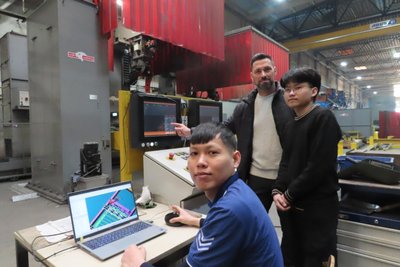 Quoc Khanh Vo (links) und Quyet Huu Nguyen mit Ausbilder André Dietz an einem der Schweißroboter in der Aufliegerproduktion.