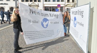 Sandra Eberbach und Anja Ksienzyk von der Stadtverwaltung Freiberg haben am Mittwoch zwei Friedensbanner an einem Bauzaun nahe des Bürgerhauses am Obermarkt angebracht. 