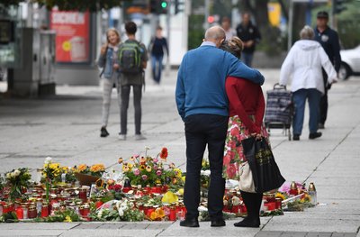 Passanten stehen am Tatort an der Brückenstraße, an dem zahlreiche Blumen und Kerzen niedergelegt wurden. 