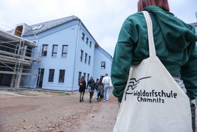 Schüler und Schülerinnen vor dem neuen Gebäude, das nach den Herbstferien für den Unterricht genutzt wird. In die alte Industriehalle nebenan (links) werden in den kommenden Monaten unter anderem eine Schmiede, eine Weberei und Ateliers eingebaut. 