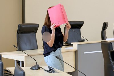 Die Angeklagte betritt den Gerichtssaal mit rotem Aktendeckel vor dem Gesicht.