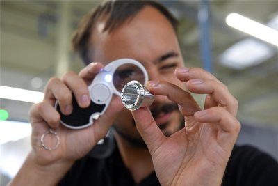 Zerspanungsmechaniker Eric Ludwig checkt mit Lupe und Lampe die Oberfläche eines Bauteils.