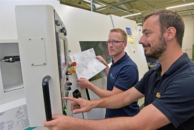 Geschäftsführer Manuel Hüttel richtet mit Zerspanungsmechaniker Eric Ludwig, rechts, eine CNC-Bearbeitungsmaschine ein. Über 30 dieser Automaten bilden das Rückgrat.