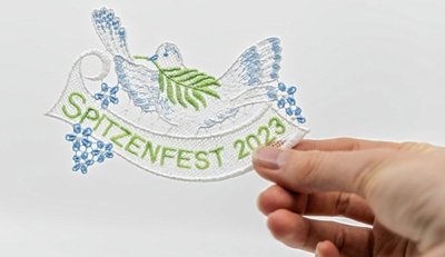 Das diesjährige gestickte Spitzenfestabzeichen zeigt eine Friedenstaube. 